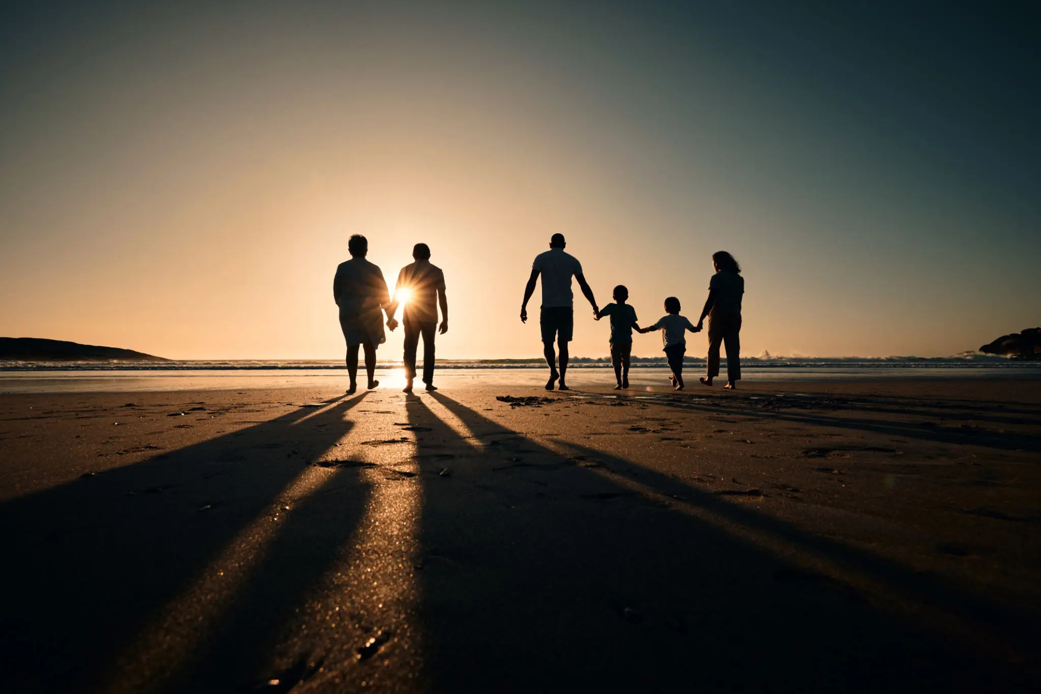 Family walking on beach at sunset.