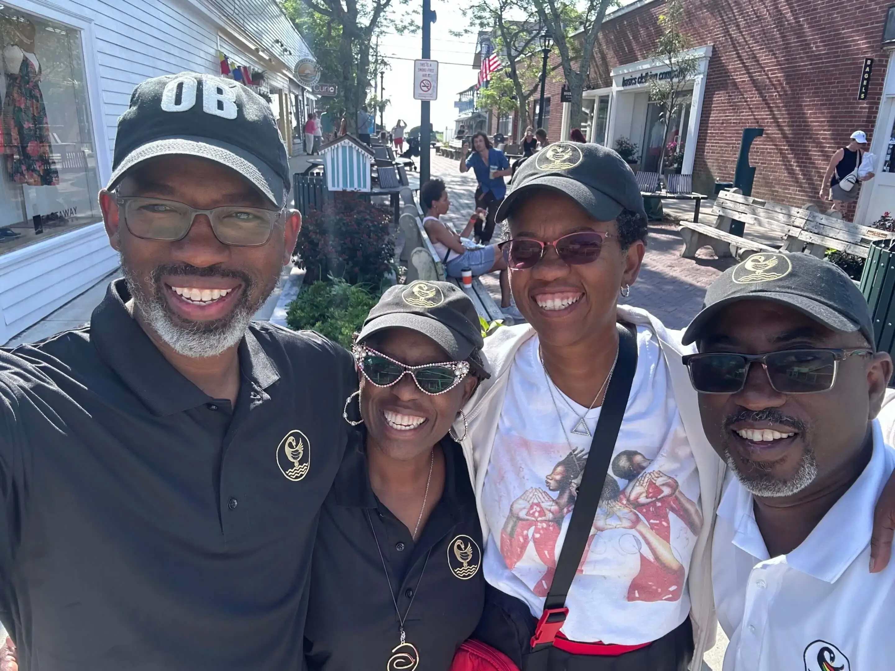 Four people smiling outdoors, wearing casual caps and shirts.
