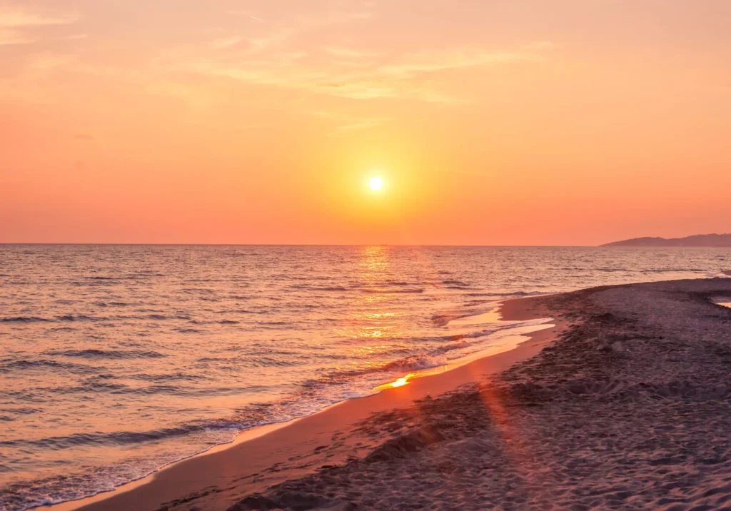 Sunset over a calm beach with gentle waves.