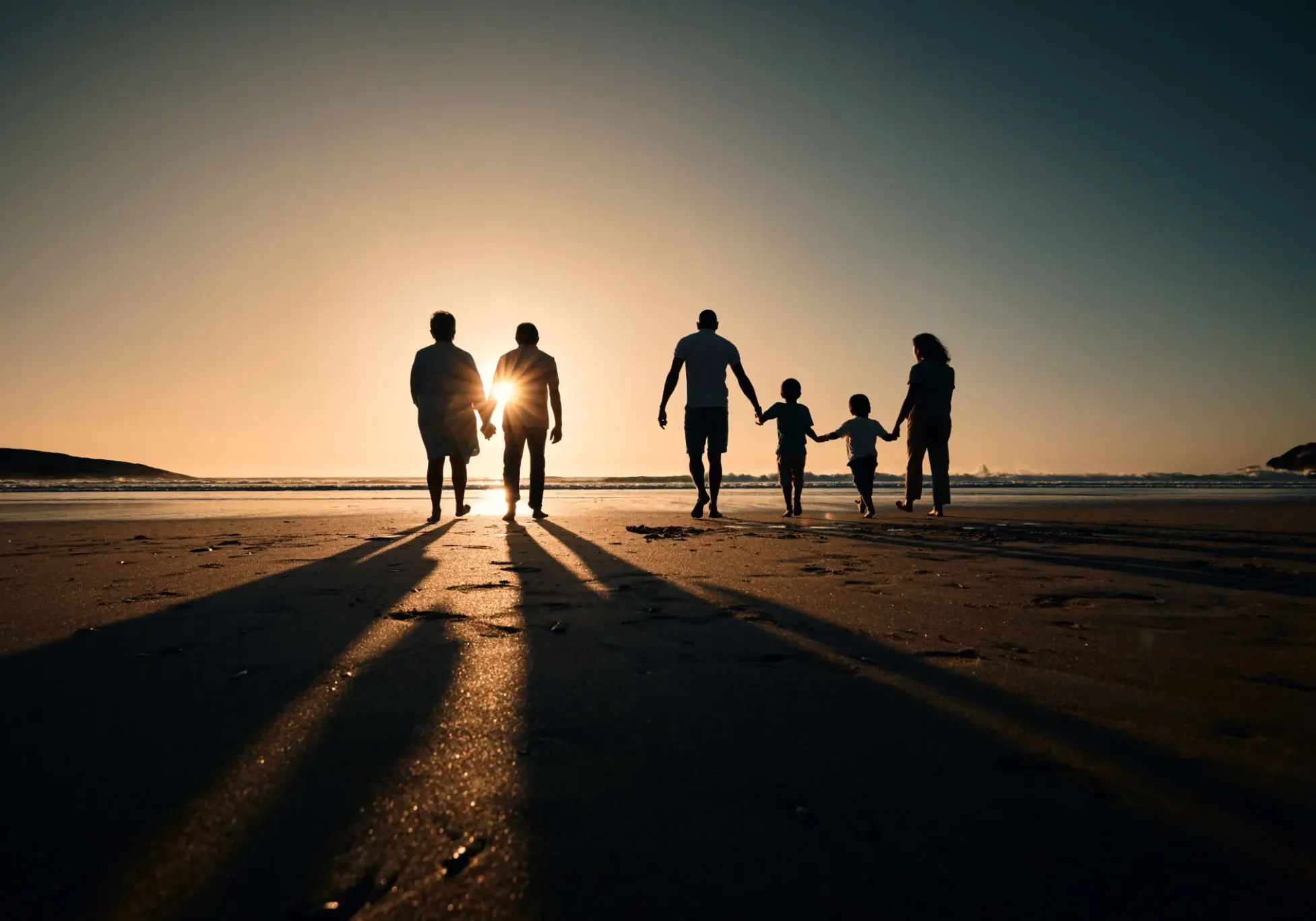 Family walking on the beach at sunset with long shadows.